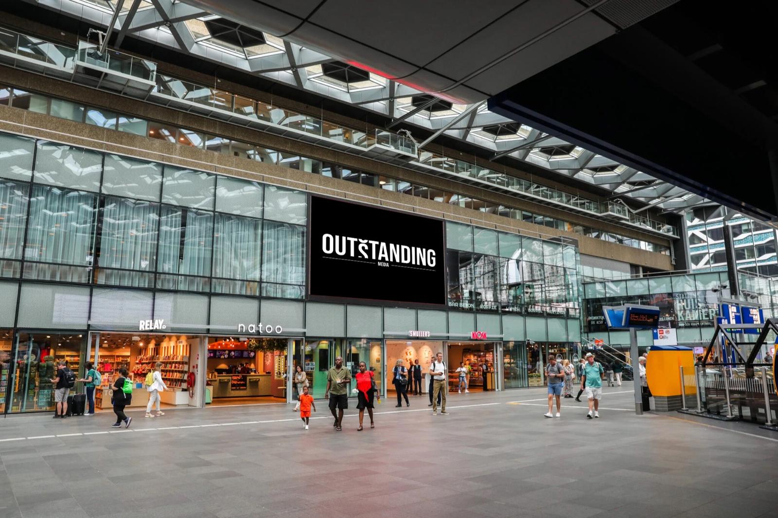 Groot digitaal scherm boven de winkels in een drukke stationshal met reizigers